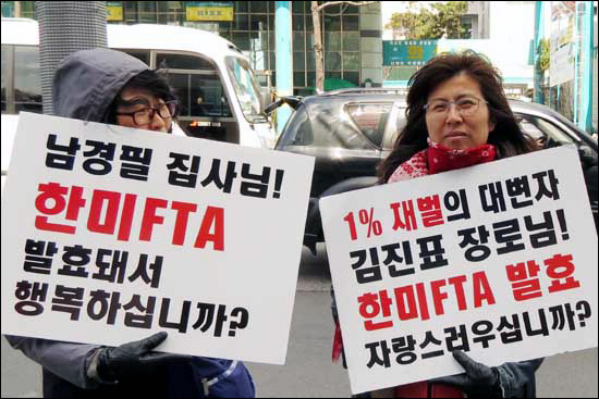 다산인권센터 박진 상임활동가(오른쪽)가 "1% 재벌의 대변자 김진표 장로님! 한미FTA 발효 자랑스러우십니까?"라고 적힌 손팻말을 들고 서 있다.