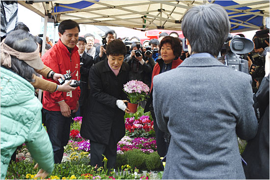 꽃가게 천막 안에서 김진태 후보로부터 꽃 화분을 선물받은 뒤, 카메라를 향해 또 다른 포즈를 취하고 있는 박근혜 선대위원장.