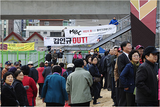 박근혜 선대위원장이 시장을 빠져나가는 모습을 물끄러미 바라보는 시민들. 그 뒤에 걸려 있는 '김인규 OUT' 'MBC를 국민의 품으로...' 플래카드.