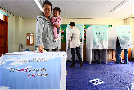 부평구 여성 유권자가 아이를 안은 채 4.11 총선 투표용지를 투표함에 넣고 있다.