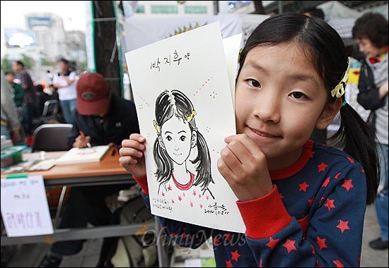 11일 오후 서울 중구 대한문 앞에서 열린 '쌍용자동차 희생자들을 돕기위한 후원 바자회'에서 한 아이가 자신의 얼굴이 그려진 캐리커처를 받고 만족하고 있다.