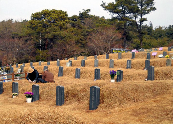 민주열사의 묘소에서 한 부부가 무덤가의 잡초를 뽑고 있는 모습.