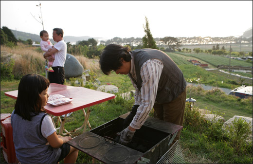 김성호 씨가 펜션에서 손님이 고기를 구울 수 있도록 숯불을 피워주고 있다. 저만치 보이는 솔밭이 지리해수욕장이다.