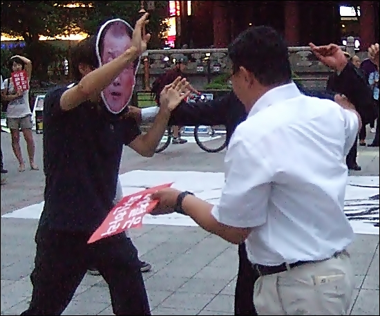 <'쫌, 보자 무한도전×2'> 프로젝트 9일차 캠페인에서 김재철 사장의 사진탈을 쓴 시민이 시민들에게 잡혀 응징을 당하고 있다. 