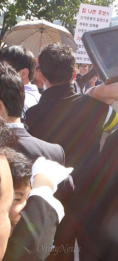 21일 경남 김해 봉하마을을 방문한 박근혜 새누리당 대통령후보가 경호원들에 둘러싸인 채 노무현 전 대통령 묘역을 나서고 있다. '선거운동의 일환으로 계획된 참배'라며 박 후보의 묘역 참배를 거부하는 한 시민의 피켓이 뒤로 보인다.