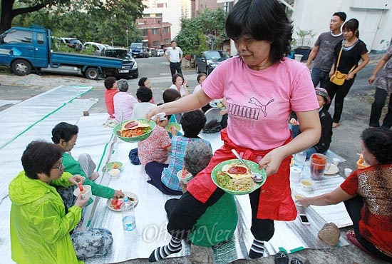 6일 오후 서울 은평구 신사2동 팔각정에서 산새마을 주민 주최로 '별이 빛나는 영화제'가 열릴 가운데, 마을 주민들이 영화를 관람하기 위해 모인 주민들에게 비빔밥을 나눠 주고 있다.