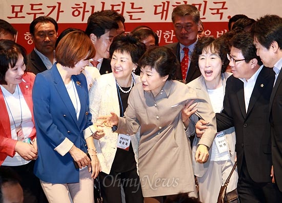 박근혜 후보가 참석자들과 기념촬영을 하는 가운데, 일부 참석자들이 박 후보의 팔을 끌어 당기고 있다.