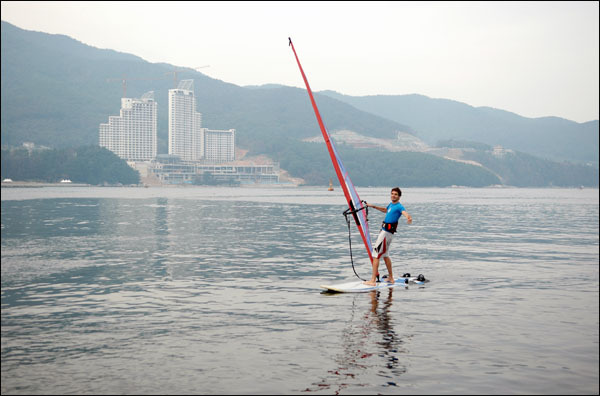 윈드서핑은 낭만을 가득 싣고 지세포항을 가로지르며, 그림 같은 풍경을 연출하고 있다. 뒤로 보이는 하얀 건물은 거제대명리조트 공사현장으로, 내년 상반기에 준공할 예정이다.