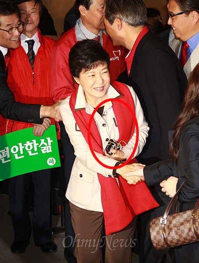 박근혜 후보가 핀 마이크를 옷에 착용한 채 손에는 아이폰과 무선송신기를 든 채 행사장에 입장하고 있다.