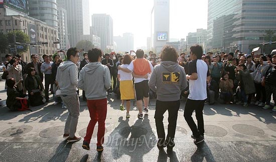 광화문광장에 모인 팬들이 제자리뛰기 퍼포먼스 '정봉런'  중인 멤버들의 모습을 사진에 담고 있다.