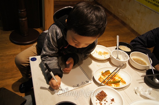  한 어린이가 희망식당에서 밥을 먹은 후 '맛있어요'라고 방명록을 쓰고 있다.