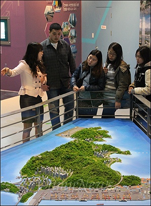 부산광역시청 1층에 위치한 미래도서관(홍보관)에서 관람객들이 직원의 안내를 받으며 가덕 신공항 모형을 지켜보고 있다. 