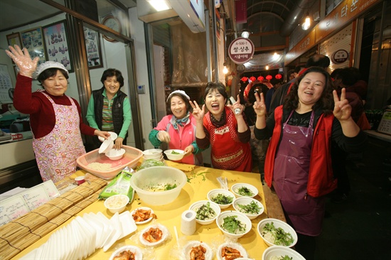  남문시장 진흥조합의 여성상인회 회원들이 먹거리 장터에서 국수를 준비하며 촬영을 위해 활짝 웃고 있다. 