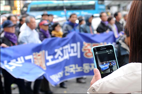 '전태일 열사 정신 계승! 2012 전국노동자대회'에 참가한 민주노총 노조원들이 서울역까지 행진을 펼치고 있는 가운데 한 외국인이 스마트폰을 이용해 노동자들의 행진모습을 사진 찍고 있다.