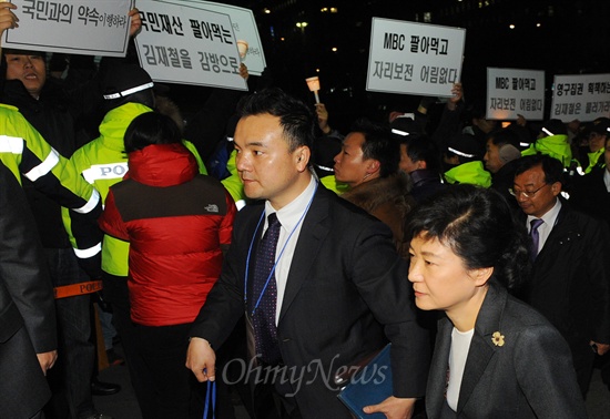  박근혜 새누리당 대선후보가 12월 4일 오후 서울 여의도 MBC에서 중앙선거관리위원회가 주최하는 첫 번째 대선 후보 TV토론회에 참석하기 위해 입장하고 있는 가운데, MBC 노조원들이 김재철 사장 퇴진 등을 촉구하며 피켓시위를 하고 있다. 