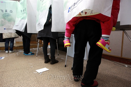 한 할머니가 어린아이를 업고 기표소에서 투표를 하고 있다.