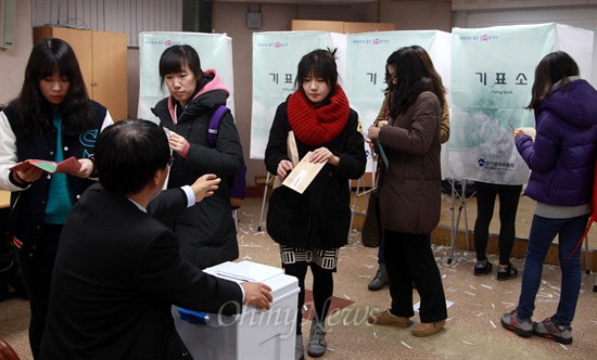 젊은 유권자들이 기표소에서 나와 투표함에 봉인된 부재자투표 봉투를 넣고 있다.