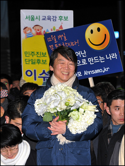 안철수 전 후보가 제18대 대통령선거를 하루 앞둔 18일 저녁 서울 강남역사거리에서 민주통합당 문재인 후보의 지원유세를 펼치고 있는 가운데 한 유권자로부터 받은 꽃다발을 들고 있다