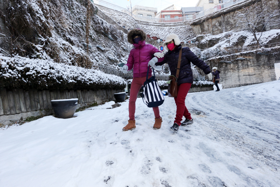 밤새 많은 양의 눈이 내린 12월 30일 오전 서울 이화마을에서 관광객들이 빙판길을 힘겹게 내려오고 있다.