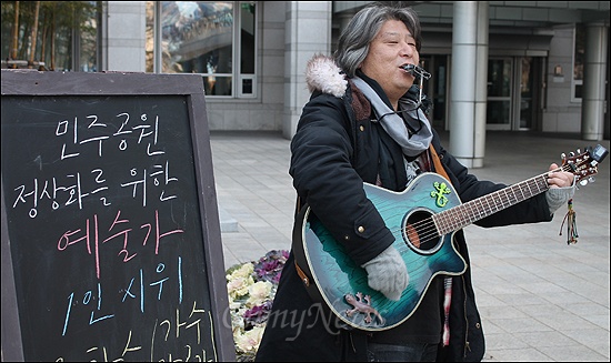  부산시의회의 부산민주공원 예산 삭감에 반대하는 1인 시위가 8일부터 오는 2월 5일까지 부산시의회에서 진행된다. 8일 낮 12시부터 1인 시위에 나선 음악인 우창수씨가 기타 반주에 맞춰 노래를 부르고 있다. 