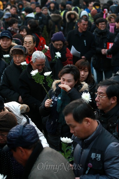 국화꽃을 든 참석자들이 사망한 철거민들의 영정에 헌화하기 위해 길게 줄을 서 있다.