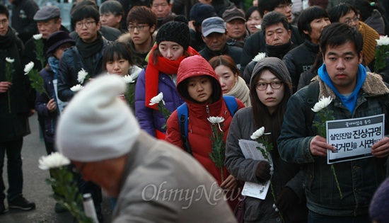 국화꽃을 든 참석자들이 사망한 철거민들의 영정에 헌화하기 위해 길게 줄을 서 있다.