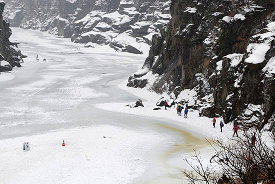 고석정에서 내려가 본 한탄강. 바위 절벽 아래 얼음이 단단히 얼어붙은 곳으로 사람들이 걸어가고 있는 모습이 보인다.