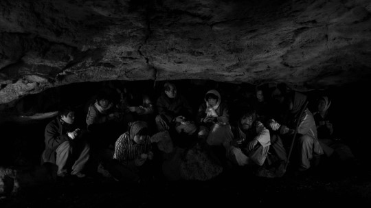 <지슬>의 한 장면. 주민들이 동굴 안 어둠 속에 옹기종기 모여 앉아있다.