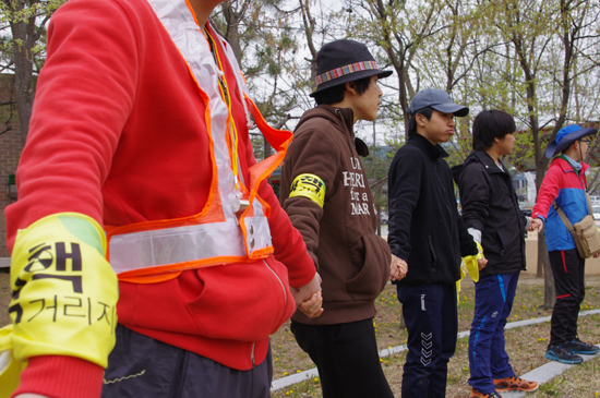 핵핵거리지마 로고가 새겨진 노란손수건을 팔에 맨 성미산학교 친구들이 엘름댄스를 추기 위해 손을 맞잡고 원을 그리고 있다.