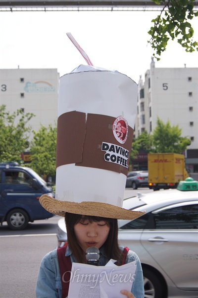 대구청년유니온의 한 회원이 커피전문점 일회용 컵 모양의 모자를 쓰고 최저임금 위반에 대해 이야기하고 있다.