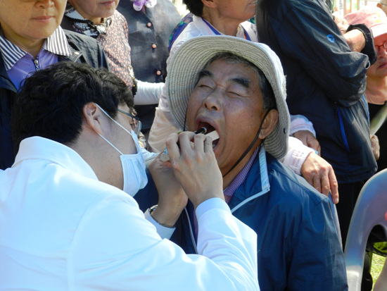 구취가 납니까? 구강검진 중인 치과의사와, 잘 볼 수 있도록 한껏 입 벌린 어르신