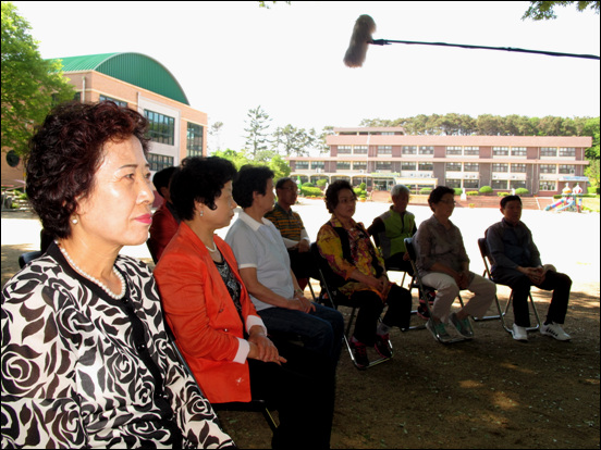 갈현초등학교 교정 정자나무 그늘 아래서 방송 촬영에 임하고 있는 동창들 모습.