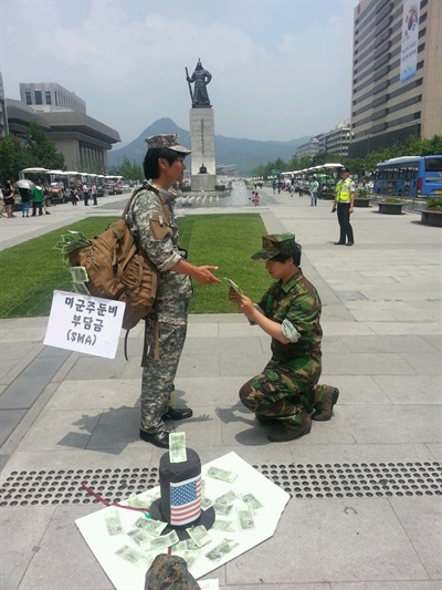  '평화와 통일을 여는 사람들'은 서울 광화문 광장에서 지난 5월 22일 '불법부당한 방위비분담금(미군주둔경비)를 위해 미군에게 국민혈세 갖다 바치는 한국 정부당국을 풍자' 퍼포먼스를 펼쳤다.