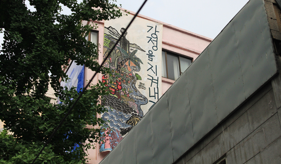2013년 6월 30일 오후, 평화박물관 스페이스99 앞에서 건물에 걸려 있는 걸개그림 '강정을 지켜내자'를 찍었다. 이 그림은 파견미술가 팀의 공동 작품이다.