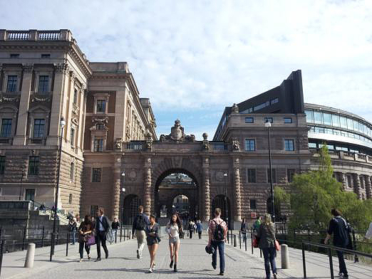 스웨덴 국회의사당, 의사당 가운데 길이 나있고 그 길 양 끝에 개선문이 건물과 건물을 잇고 있다. 그리고 사람들이 그 길을 활보한다.