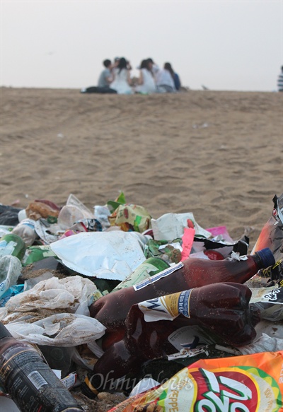 11일 이른 아침까지 술자리를 갖고 있는 피서객들과 다른 피서객들이 버려놓고 간 쓰레기 더미. 이날 해운대해수욕장에서는 모두 7.5톤의 쓰레기가 수거됐다. 
