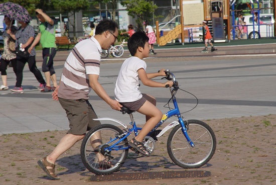 아빠가 자전거 뒤에서 아들 넘어지지 않도록 자전거 힘껏 붙잡고 뜁니다.