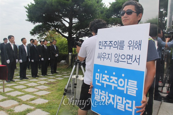 무소속 안철수 국회의원이 1일 부산 민주공원을 분향소인 '추념의장'에 참배하는 동안 한 시민이 "민주주의를 위해 싸우지 않으면서 민주주의를 말하지 말라"는 내용의 피켓을 들고 1인시위를 벌이고 있다.