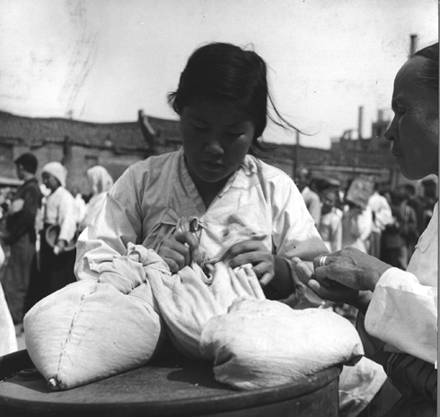 한 피난민이 5일 분 양곡을 배급받은 뒤 자루를 묶고 있다(1951. 5.). 
