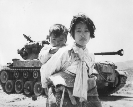 한 소녀가 동생을 업은 채 전차 앞에 서 있다(경기도 행주, 1951. 6. 9.).