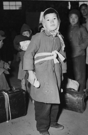 피난지 부산에서 다시 남해안 섬으로 가는 배를 기다리는 피난민들 가운데 동생을 업은 소녀.(1951. 2. 8.).