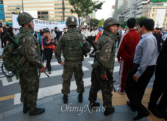 평화와통일을여는사람들(평통사) 회원들이 '건군 제65주년 국군의 날' 기념 시가행진이 열리는 1일 오후 서울 세종로 네거리에서 '전시작전통제권 환수' 촉구 시위를 벌이고 있다. 시가행진 도중 벌어질 만일의 사태에 대비해 배치된 군인들이 시위 장면을 지켜보고 있다.