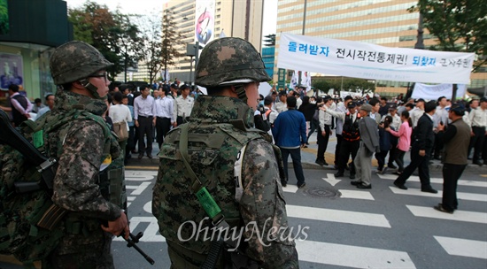 평화와통일을여는사람들(평통사) 회원들이 '건군 제65주년 국군의 날' 기념 시가행진이 열리는 1일 오후 서울 세종로 네거리에서 '전시작전통제권 환수' 촉구 시위를 벌이고 있다. 시가행진 도중 벌어질 만일의 사태에 대비해 배치된 군인들이 시위 장면을 지켜보고 있다.