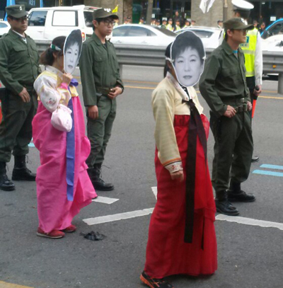박근혜 대통령 가면을 쓰고 한복을 입은 여성 참가자가 행진하고 있다. 