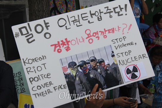  한국전력공사가 밀양 송전탑 공사를 재개한지 엿새째인 7일 낮 12시경 주민들이 밀양시 단장면 단장리 소재 '송전선로 공사장비 적치장' 앞에서 농성하면서 '복면 경찰'에 항의하는 피켓을 들고 있다.