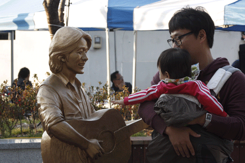 쌈지공원에 새겨진 김광석 동상의 모습. 한 시민이 어린 아이와 함께 김광석 동상 가까이에서 그를 바라보고 있다.