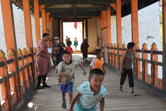 전통양식으로 만든 목조 다리에서 뛰어노는 부탄의 어린이들. 뒤로는 전통 복장을 한 사람이 보인다. 