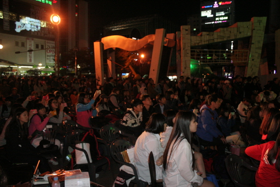 부평역 쉼터공원에서 열린 청소년 문화 콘서트 <출구>를 보며 즐기고 있는 사람들. 100여 명의 사람들이 모여 있다.