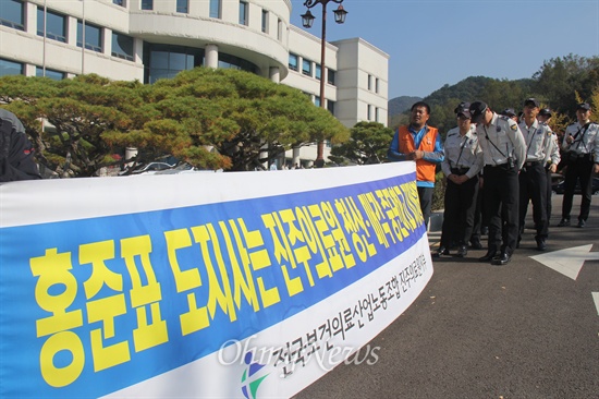  전국보건의료산업노동조합이 경남도의회 정례회 개회에 맞춰 5일 오후 2시경 홍준표 지사가 지나가기에 앞서 진주의료원 재개원을 촉구하는 내용으로 피켓을 들고 서 있자 경찰이 지켜보고 있다.