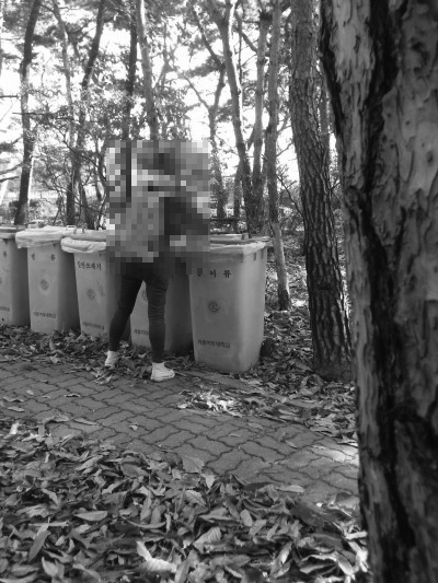 한 여학생이 대학내에 위치한 쓰레기통에 쓰레기를 버리고 있다. 